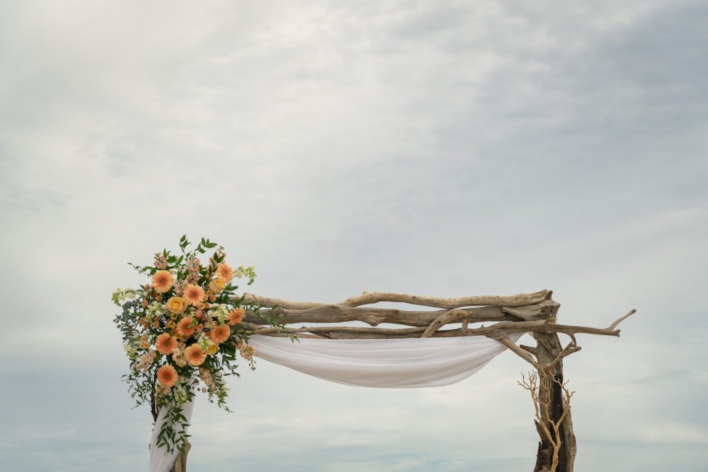 a wooden arch with a white drape and orange flowers