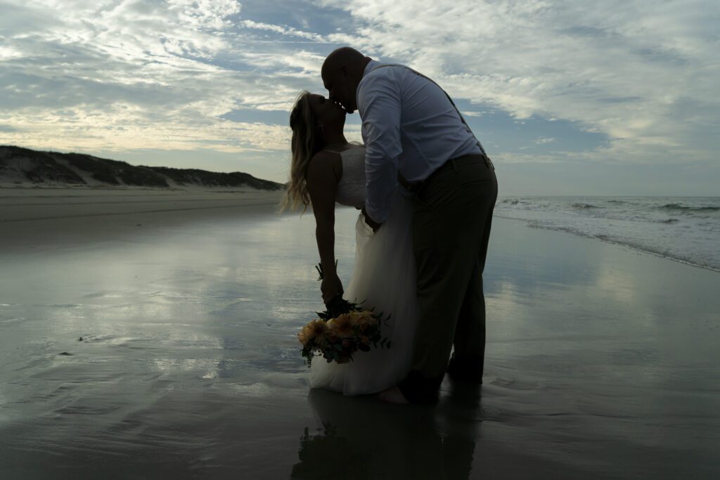 a bride and groom kissing on the beach