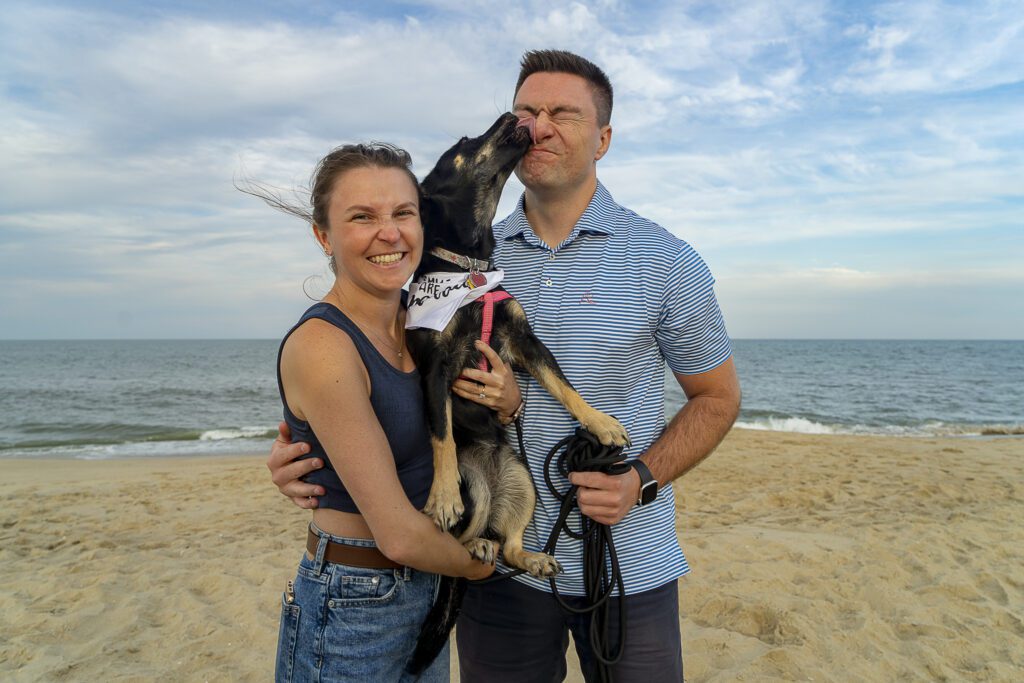 a man and a woman standing on a beach with a dog