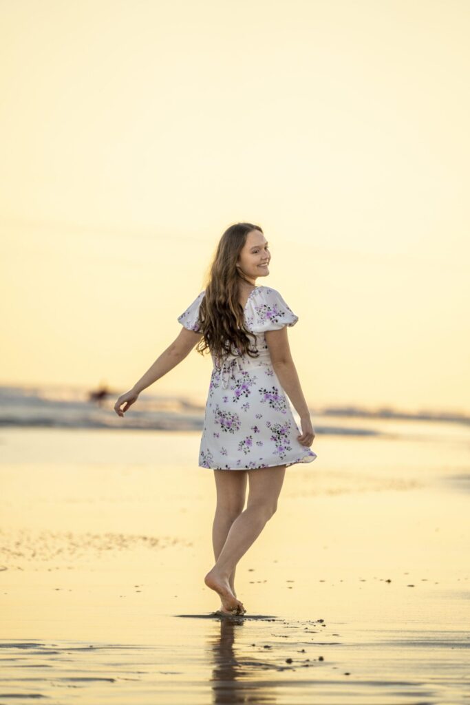 a woman walking along a beach at sunset